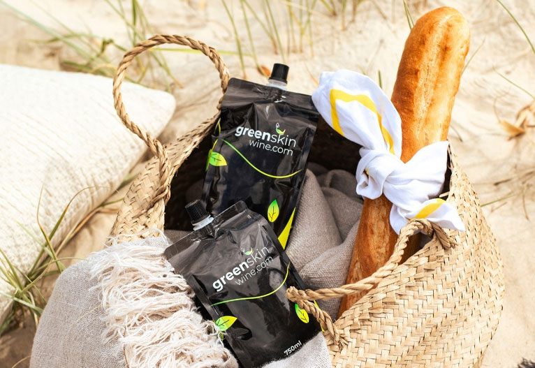 Basket containing wine bags and baguette at the beach.