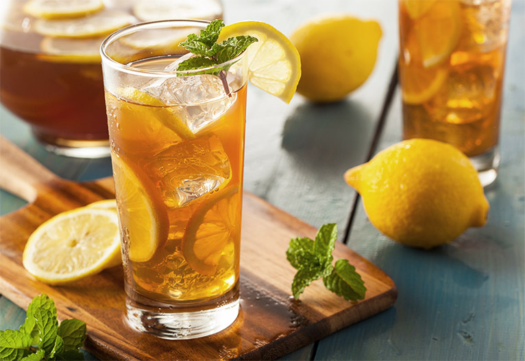 Sparkling tea in a tall glass with ice and lemon.