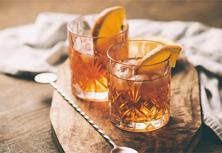 Two whiskey cocktails with citrus wedges.