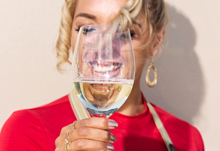 Woman holding up a glass of wine in front of her face.