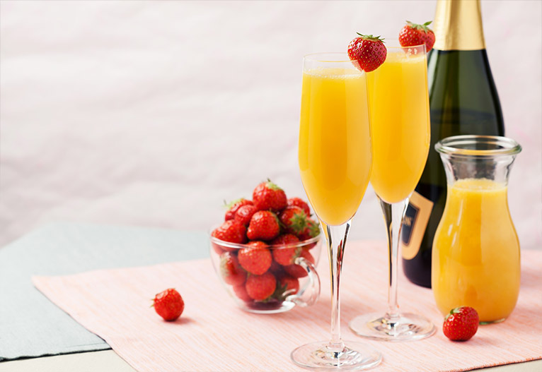 Mimosas with a bottle of champagne and a bowl of strawberries.