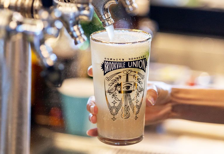 Person pouring a ginger beer into a glass from a bar tap.