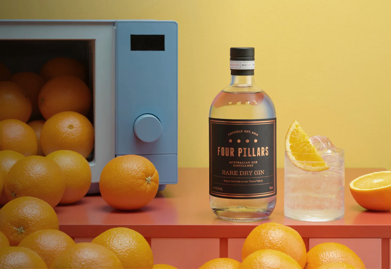 Four Pillars Rare Dry Gin bottle on a table with oranges and a glass.