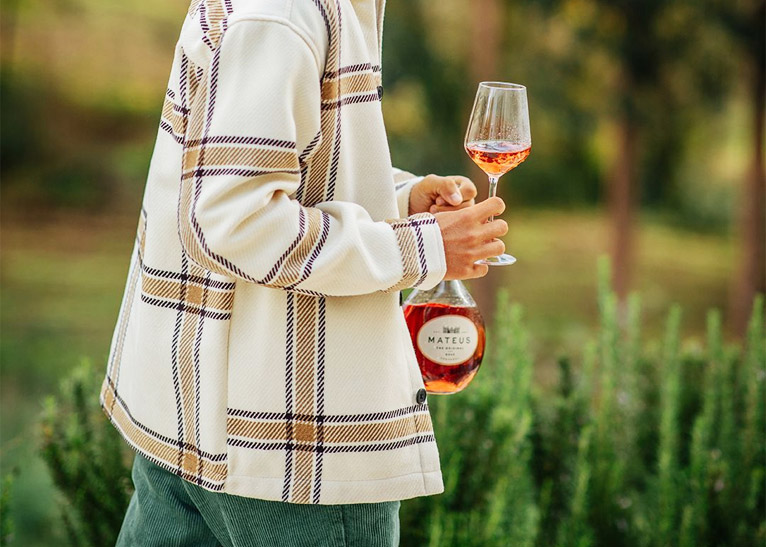 Person walking and holding a bottle of wine and a glass.