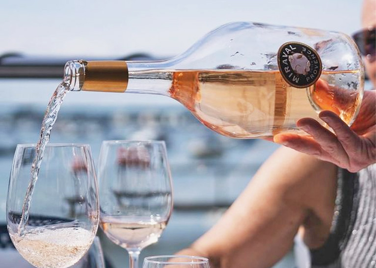 Person pours Miraval Rosé Wine into glasses near the sea.