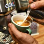 Person pouring milk into an espresso.