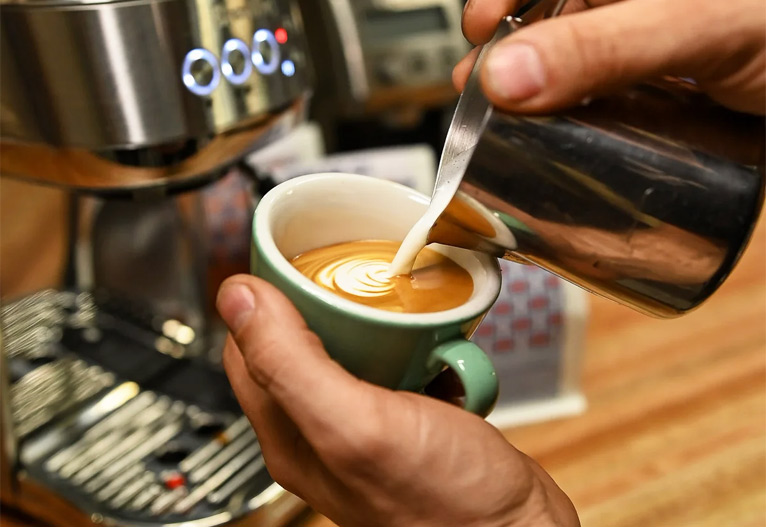 Person pouring milk into an espresso.