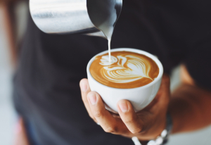 Person pouring milk into a cup of coffee.