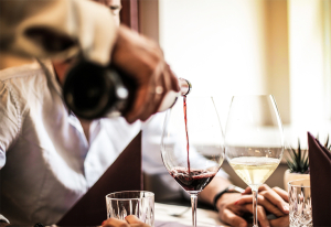 Waiter pouring red wine into a glass at a table.