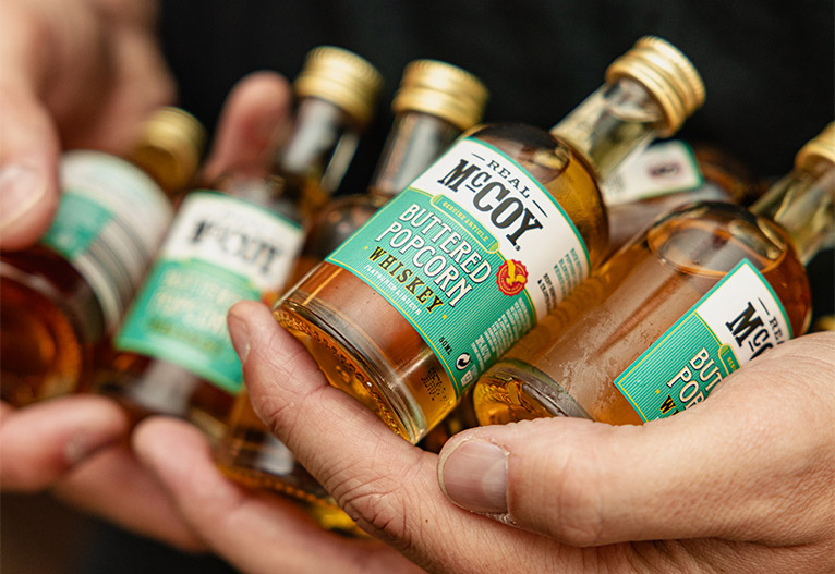 Man holds Real McCoy Flavoured Whiskey mini bottles.