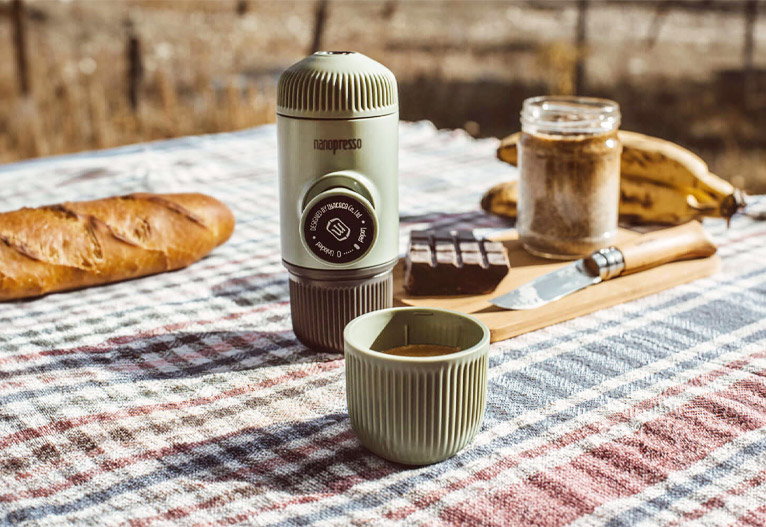 Wacaco Nanopresso manual coffee maker in green on a picnic rug.