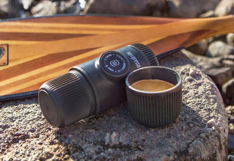 Wacaco Nanopresso manual coffee maker on a rock next to a mug.