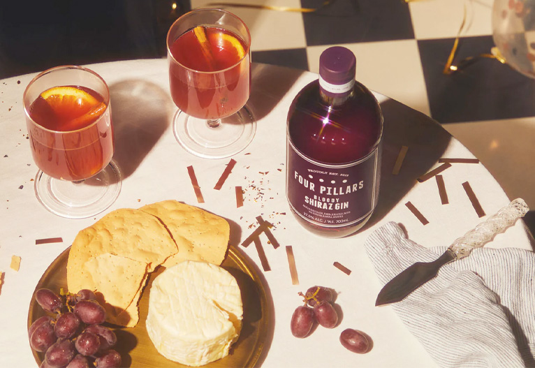 Four Pillars Bloody Shiraz Gin on a table with a cheese platter and cocktails.