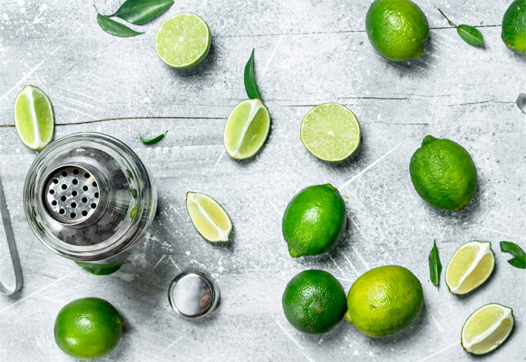 A cocktail shaker and fresh limes on a bench.
