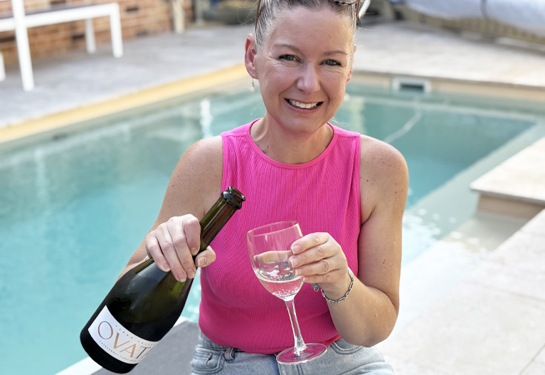 Woman pouring sparkling wine next to a pool.