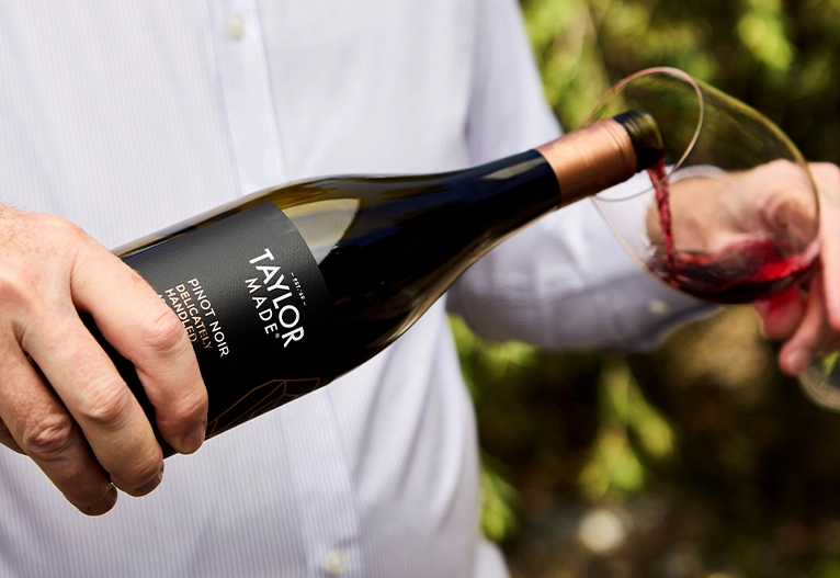 Person pouring a bottle of Taylor Made Pinot Noir 2024.