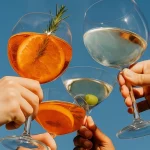 Hands holding up Lyres Zero-Alcohol cocktails in glasses.