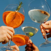 Hands holding up Lyres Zero-Alcohol cocktails in glasses.