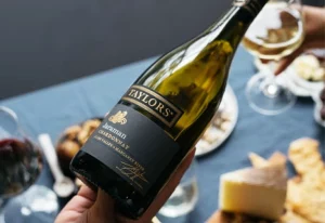 Person holding a bottle of Taylors Jaraman Chardonnay over a table.