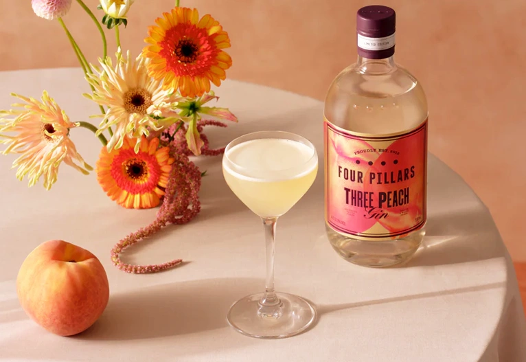 Bottle of Peach Gin on a table with a cocktail.