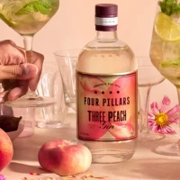 Bottle of Three Peach Gin on a table with peaches and accessories.