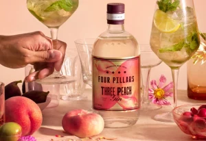 Bottle of Three Peach Gin on a table with peaches and accessories.